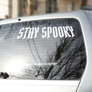 May include: A white vinyl sticker with the text "STAY SPOOKY" on a car window.