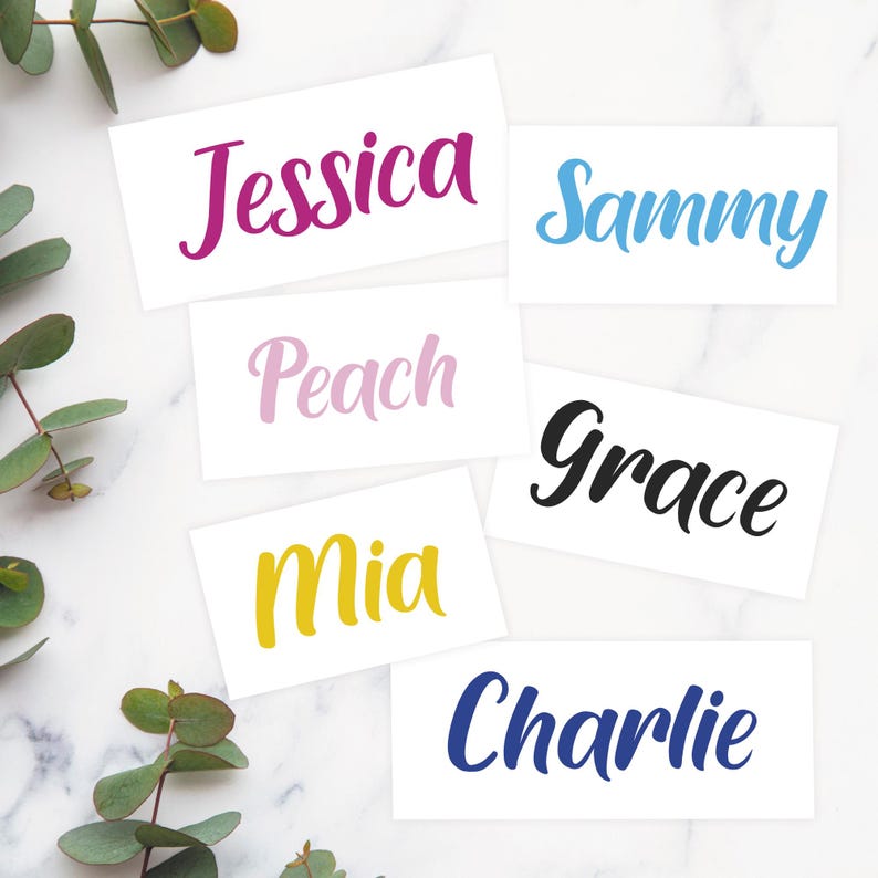 May include: White rectangular cards with names written in various colors. Names include Jessica, Sammy, Peach, Grace, Mia, and Charlie. The names are written in a cursive font. Green leaves are in the background.