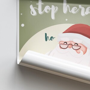 May include: A green and white Christmas sign with a cartoon Santa Claus. The sign says "Stop here ho ho ho".