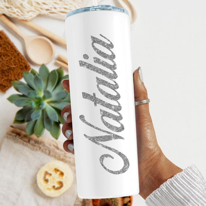 May include: White stainless steel tumbler with a silver glitter design that says "Natalia" on it.