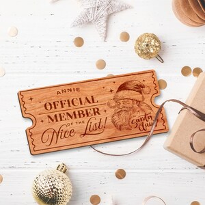 May include: A wooden ticket with a red laser-engraved design. The ticket says "Annie Official Member of the Nice List!" and features a drawing of Santa Claus with the text "Approved by Santa Claus".