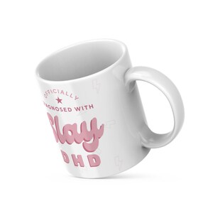 May include: White ceramic mug with a pink graphic that says "Officially Diagnosed with Slay ADHD".