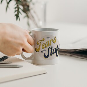 May include: White ceramic mug with a yellow and blue graphic that says "The Tears of My Staff".