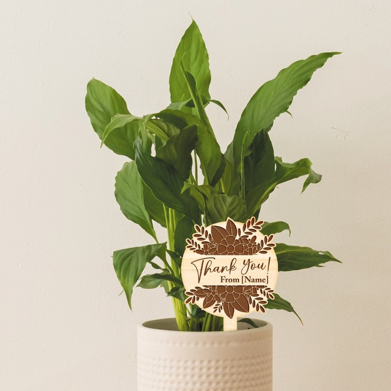 May include: A wooden plant stake with a brown floral design and the text "Thank you! From [Name]" in a white font.