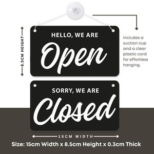 Op de afbeelding: Zwart rechthoekig bord met de woorden "HELLO, WE ARE Open" en "SORRY, WE ARE Closed" in witte letters. Het bord is 15 cm breed en 8,5 cm hoog, met een dikte van 0,3 cm. Inclusief zuignap en transparant plastic koord.