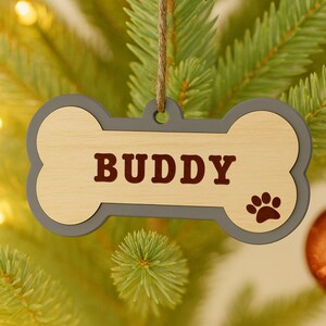 Peut inclure: Ornement en forme d'os de chien en bois avec le nom "BUDDY" en lettres marron. L'ornement a une bordure grise et une empreinte de patte. Il est suspendu &agrave; une ficelle en ficelle naturelle, parfait pour un sapin de No&euml;l sur le th&egrave;me des animaux.