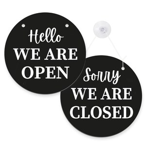 K&ouml;nnte beinhalten: Zwei schwarze, runde Schilder mit wei&szlig;em Text. Eines sagt "Hello WE ARE OPEN", das andere sagt "Sorry WE ARE CLOSED". Die Schilder sind durch eine wei&szlig;e Schnur und einen Saugnapf verbunden.