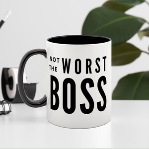 May include: White ceramic mug with a black rim and handle. The mug has black text that reads "Not the Worst Boss".