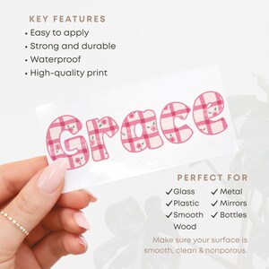 Puede incluir: Una pegatina blanca con el nombre "Grace" en letras de cuadros rosas con detalles florales. La pegatina est&aacute; sujeta por una mano. El texto indica que es f&aacute;cil de aplicar, fuerte, duradero, impermeable y de alta calidad.