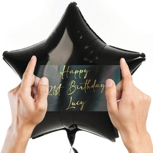 May include: A black star-shaped balloon with a clear sticker that says "Happy 21st Birthday Lucy" in gold lettering.