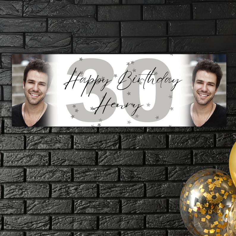 May include: A personalized birthday banner with the text "Happy Birthday Henry" and the number "30" in gray. The banner includes two photos of a smiling man. The background is a black brick wall.