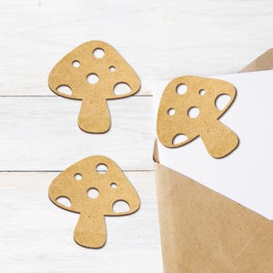 以下が含まれることがあります： 白い木製の表面に、白い点のある茶色の木製のキノコの形が3つあります。キノコは切り抜かれており、裏側は平らです。