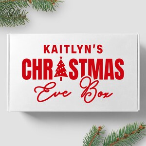 May include: White box with red text that reads "Kaitlyn's Christmas Eve Box". A red Christmas tree icon is above the word "Christmas".