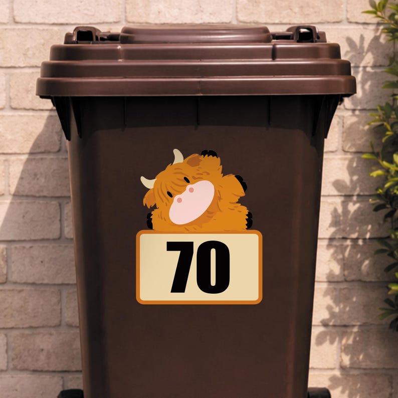 May include: A brown trash bin with a brown lid. A sticker of a cartoon Highland cow is on the bin, with the number 70 on a rectangular sign below the cow.