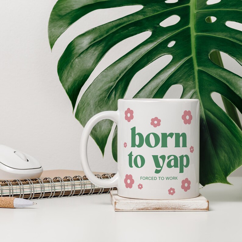 May include: White ceramic mug with a green and pink design. The mug says "born to yap" with the words "forced to work" in smaller text below.