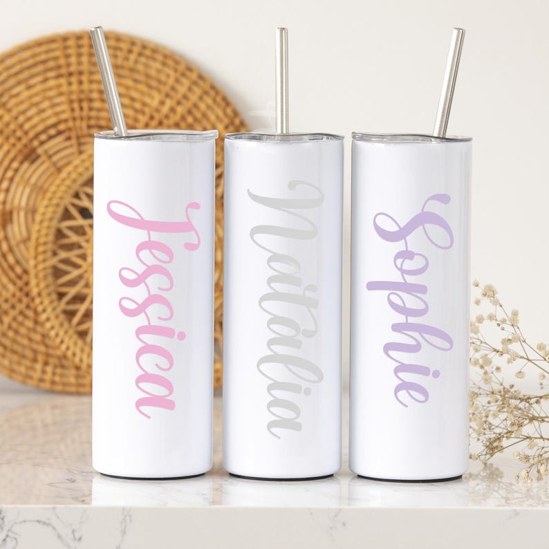 May include: Three white stainless steel tumblers with personalized names, "Jessica", "Matilda", and "Sophie", in pink, gray, and purple lettering. Each tumbler has a matching straw.