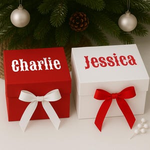 May include: Two gift boxes, one red and one white, are displayed. The red box has the name "Charlie" in white script, and a white bow. The white box has the name "Jessica" in red script, and a red bow. A Christmas tree is in the background.