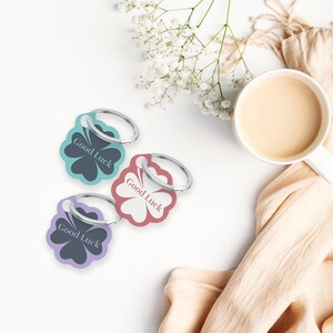 May include: Three silver keyrings with four-leaf clover charms. Each charm has the text "Good Luck" in black lettering. The charms are teal, purple and pink.