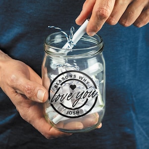May include: A glass jar filled with rolled up pieces of paper with a black and white sticker on the front that says "Reasons Why I Love You Josh" with a heart in the middle.
