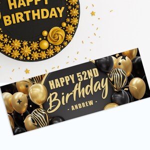 May include: A black and gold birthday cake with the words "HAPPY BIRTHDAY" in gold lettering. A banner with "HAPPY 52ND BIRTHDAY - ANDREW -" is surrounded by black and gold balloons. Gold stars and confetti are scattered around.