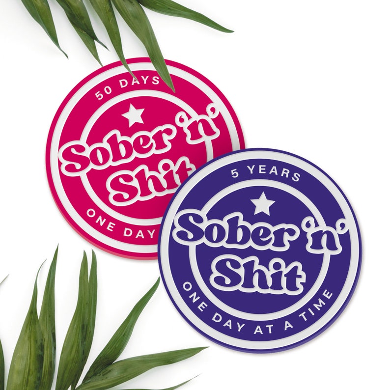 Puede incluir: Dos posavasos redondos con texto blanco sobre un fondo colorido. El posavasos rosa dice "50 D&Iacute;AS Sobrio y Mierda UN D&Iacute;A" y el posavasos morado dice "5 A&Ntilde;OS Sobrio y Mierda UN D&Iacute;A A LA VEZ".