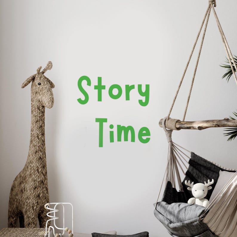 May include: A white wall with the words "Story Time" written in green letters. A brown woven giraffe toy stands on the left side of the image. A hanging hammock chair with a gray cushion and a white stuffed reindeer toy is on the right side of the image.