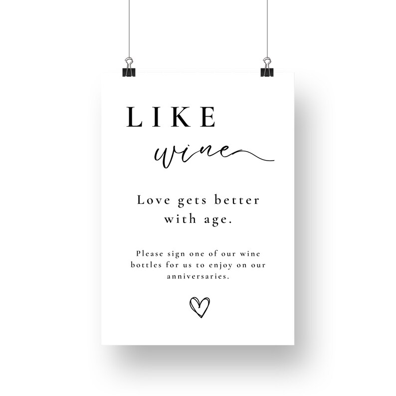 May include: A white sign with black text that reads "LIKE wine Love gets better with age. Please sign one of our wine bottles for us to enjoy on our anniversaries." There is a small heart at the bottom of the sign.