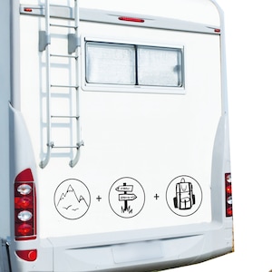 K&ouml;nnte beinhalten: Ein wei&szlig;er Wohnwagen mit drei schwarzen und wei&szlig;en Aufklebern auf der R&uuml;ckseite. Die Aufkleber zeigen eine Bergkette, einen Wegweiser mit Pfeilen, die in verschiedene Richtungen zeigen, und einen Rucksack.