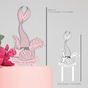 May include: Pink and gray mermaid cake topper with a shell, starfish, and waves. The topper is 14.2 inches tall and 9.1 inches wide. The topper says "Millie's 5th Birthday".