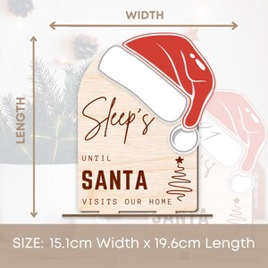 May include: Wooden sign with a red Santa hat, a Christmas tree, and the text "Sleep's Until Santa Visits Our Home". The sign measures 15.1 inches wide by 19.6 inches long.