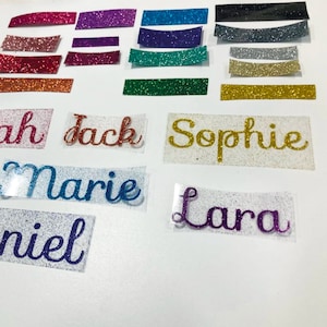 May include: A selection of glitter name decals and glitter strips in various colours. Names include "Sarah", "Jack", "Sophie", "Marie", "Daniel", and "Lara". Glitter colours include red, gold, blue, purple, and green.