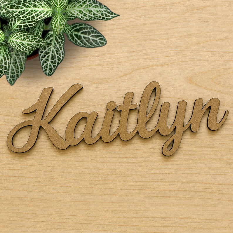 May include: A wooden sign with the name "Kaitlynn" written in cursive script. The sign is a light brown color and is made of wood.
