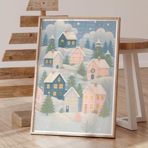 May include: A framed print featuring a winter village scene. The artwork depicts colorful houses nestled in a snowy landscape, with evergreen trees and a starry sky. The houses are in shades of blue and pink, with wreaths on some doors.