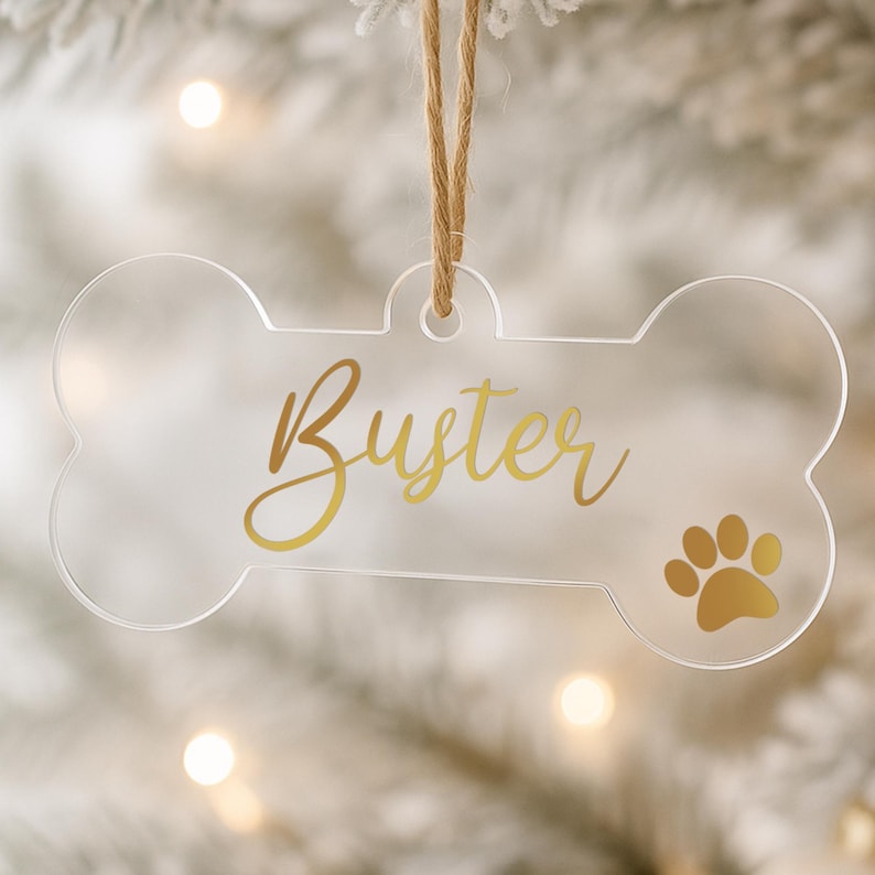 以下が含まれることがあります： 「Buster」の金色の筆記体と金色の足跡が特徴の、透明なアクリル製の犬の骨型オーナメント。 天然の麻ひもで吊り下げられており、ペット愛好家やホリデーデコレーションに最適です。