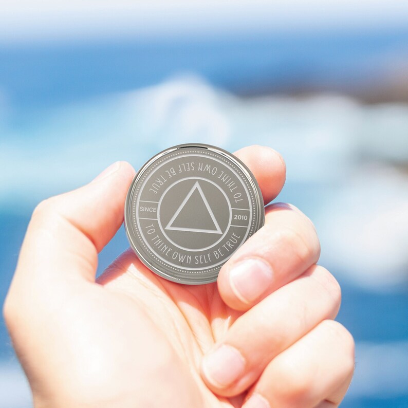 May include: A silver coin with a triangle in the center and the text "To thine own self be true" around the edge. The coin also has the text "Since 2010" on the bottom right and "To thine own self be true" on the top left.