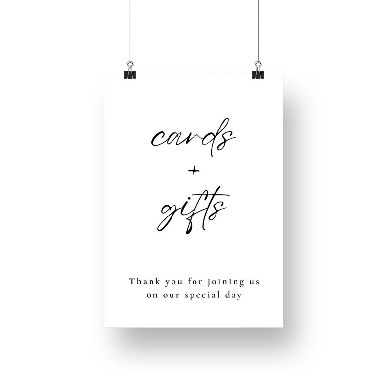May include: A white sign featuring the words "cards + gifts" in black cursive script. The text "Thank you for joining us on our special day" is below. The sign is held by two black clips.