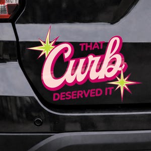 May include: A car decal with the text "That Curb Deserved It" in pink and white, with starburst accents. The decal is affixed to a black vehicle.