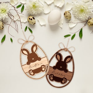 May include: Two wooden Easter egg ornaments with bunny cutouts. The ornaments are decorated with the names Anastasia and Nicholas.