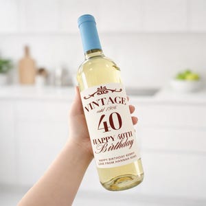 May include: A clear glass wine bottle with a light blue cap. The label reads "VINTAGE estd 1986 40 HAPPY 40TH Birthday." The bottle contains a light yellow liquid. The text "HAPPY BIRTHDAY KERRY! LOVE FROM HANNAH XOXO" is also on the label.