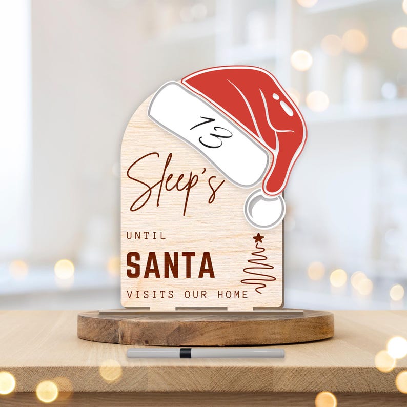 May include: A wooden countdown sign with a red Santa hat on top. The sign says "Sleep's Until Santa Visits Our Home".
