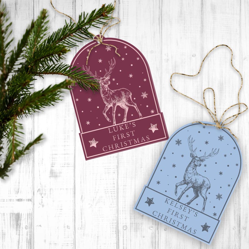 May include: Two Christmas ornaments featuring a deer design. The ornament on the left is burgundy with white snowflakes and the text "Luke's First Christmas". The ornament on the right is light blue with white snowflakes and the text "Kelsey's First Christmas".