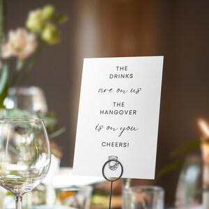 May include: White card with black text that reads "The drinks are on us. The hangover is on you. Cheers!" with a small illustration of a glass of alcohol at the bottom.