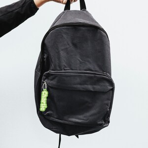 May include: A black canvas backpack with a zippered front pocket and a green keychain with the word "charlie" on it.
