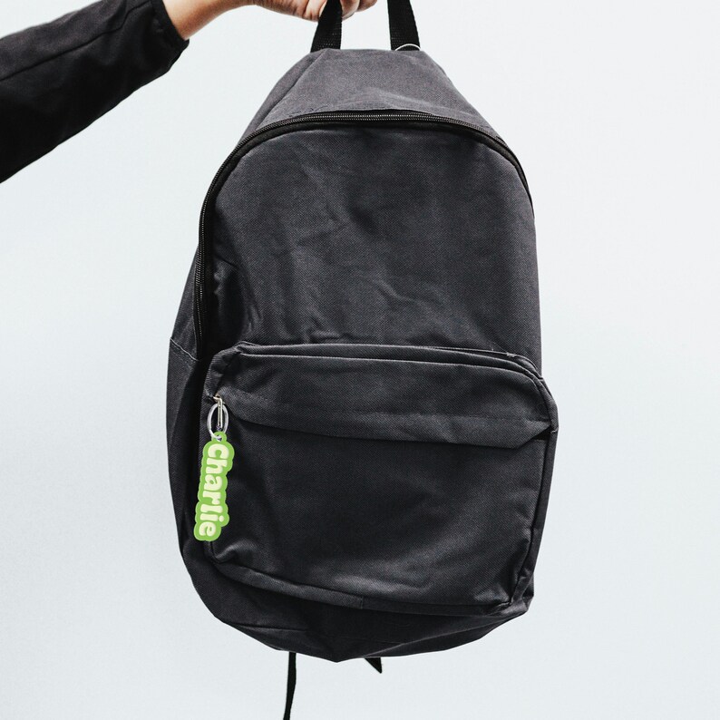 May include: A black canvas backpack with a zippered front pocket and a green keychain with the word "charlie" on it.