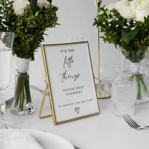 May include: Gold framed sign with the text "It's the little things. Please help yourself to whatever you may need." with a small heart symbol at the bottom.