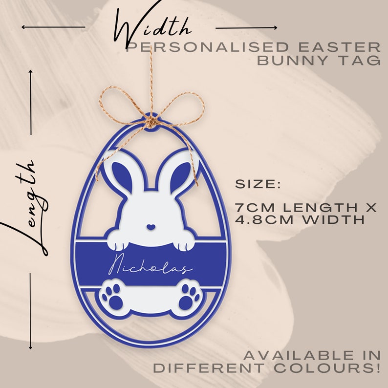 May include: A blue and white Easter bunny tag in an egg shape, personalized with the name "Nicholas." The tag is 7cm long and 4.8cm wide, with a bunny design and paw prints. The tag is suspended by a twine string. The text "PERSONALISED EASTER BUNNY TAG" is visible.
