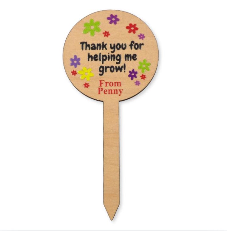 May include: A wooden garden stake with a circular top and a pointed bottom. The top features the text "Thank you for helping me grow!" and "From Penny" in black, surrounded by colorful flower illustrations.