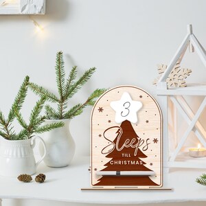 Puede incluir: Un letrero de cuenta atr&aacute;s de Navidad de madera con una estrella blanca en la parte superior que dice "3 Sleeps Till Christmas". El letrero tiene una silueta de &aacute;rbol marr&oacute;n y un marcador de borrado en seco blanco.