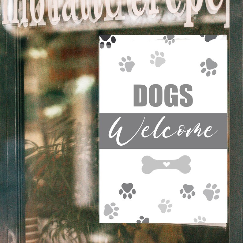 May include: A white sign with gray text and paw prints. The sign reads "DOGS Welcome" with a bone graphic. The sign is displayed on a glass door, with the word "invitation" visible at the top.
