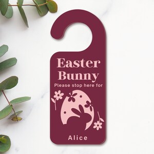 May include: Burgundy door hanger with a pink Easter bunny silhouette inside a pink egg. The text reads "Easter Bunny Please stop here for Alice".